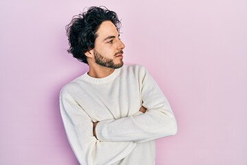 Obraz na płótnie Canvas Handsome hispanic man wearing casual white sweater looking to the side with arms crossed convinced and confident