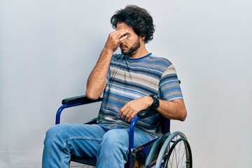 Handsome hispanic man sitting on wheelchair tired rubbing nose and eyes feeling fatigue and...