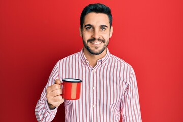 Young hispanic man holding coffee looking positive and happy standing and smiling with a confident smile showing teeth