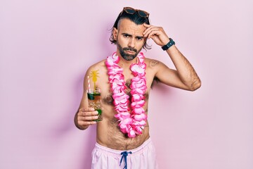 Young hispanic man wearing swimsuit and hawaiian lei drinking tropical cocktail worried and stressed about a problem with hand on forehead, nervous and anxious for crisis