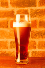 dark foamy beer in a tall glass on a wooden table against a brick wall background