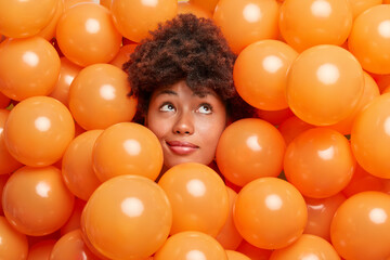 Pensive curly haired Afro American woman being at birthday party surrounded with small orange...