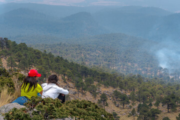 Fototapeta na wymiar A closeup shot of Hispanic hikers sitting on top of the Tlaloc Mount on a gloomy day in Mexico fire in the forest