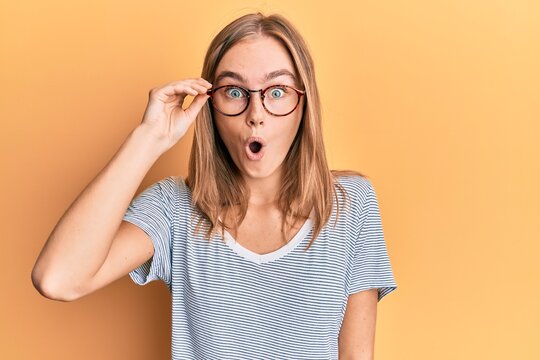 Beautiful blonde woman wearing casual clothes and holding glasses scared and amazed with open mouth for surprise, disbelief face
