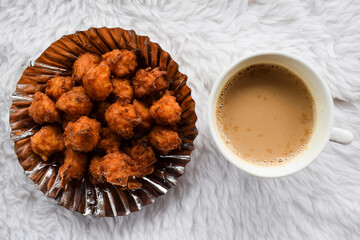 Tasty rice bhajiya or Pakoda also known as rice ball fritters is made out of Leftover rice, gram flour served in plate with hot cup of Indian masala tea or chai