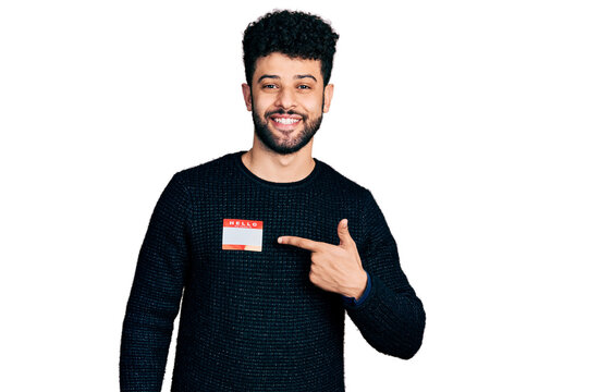 Young arab man with beard wearing hello my name is sticker identification smiling happy pointing with hand and finger