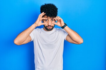 Young arab man with beard wearing casual white t shirt trying to open eyes with fingers, sleepy and tired for morning fatigue