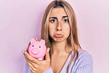 Beautiful hispanic woman holding piggy bank depressed and worry for distress, crying angry and afraid. sad expression.