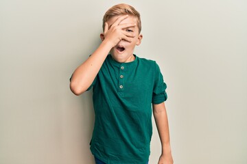 Little caucasian boy kid wearing casual clothes peeking in shock covering face and eyes with hand, looking through fingers afraid