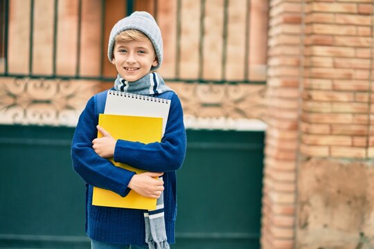 Adorable blond student kid smiling happy holding book at the school.