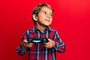 Adorable latin kid playing video game holding controller smiling looking to the side and staring...