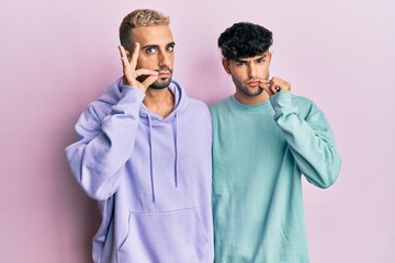 Homosexual gay couple standing together wearing casual clothes mouth and lips shut as zip with...