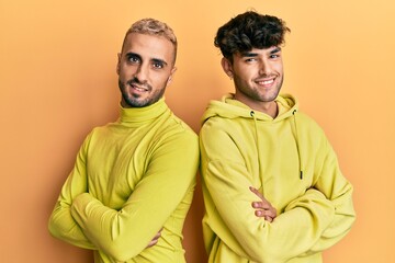 Homosexual gay couple standing together wearing yellow clothes happy face smiling with crossed arms looking at the camera. positive person.