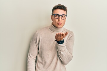 Hispanic young man wearing casual turtleneck sweater looking at the camera blowing a kiss with hand...