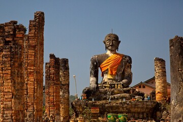 Huge stone statute of buddha looking forward wrapped in orange clock monastry Phonsavan, Laos.