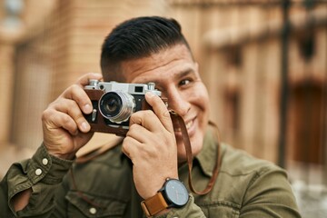 Obraz premium Young latin tourist man smiling happy using vintage camera at the city.