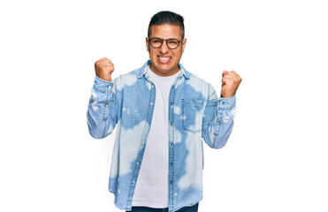Young latin man wearing casual clothes and glasses screaming proud, celebrating victory and success...