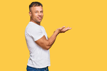 Handsome muscle man wearing casual white tshirt pointing aside with hands open palms showing copy space, presenting advertisement smiling excited happy