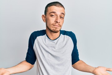 Hispanic young man wearing casual clothes clueless and confused expression with arms and hands raised. doubt concept.