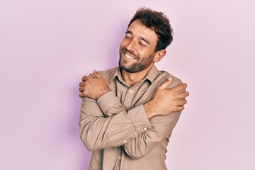 Handsome man with beard wearing casual shirt hugging oneself happy and positive, smiling confident. self love and self care