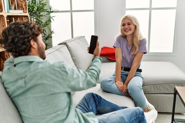 Fototapeta premium Young man making picture of his girlfriend using smartphone at home.