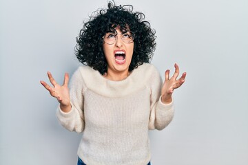 Young middle east woman wearing casual white tshirt crazy and mad shouting and yelling with aggressive expression and arms raised. frustration concept.