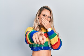 Obraz premium Beautiful young blonde woman wearing colored sweater laughing at you, pointing finger to the camera with hand over mouth, shame expression