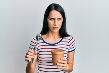 Young hispanic woman holding ice cream skeptic and nervous, frowning upset because of problem....