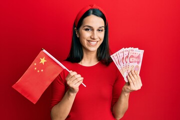 Young hispanic woman holding china flag and yuan banknotes smiling with a happy and cool smile on face. showing teeth.