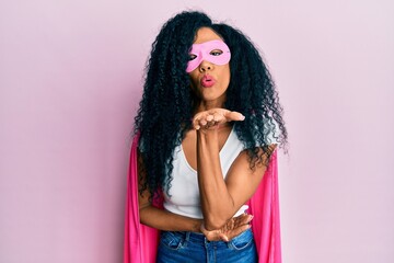Middle age african american woman wearing super hero costume looking at the camera blowing a kiss with hand on air being lovely and sexy. love expression.