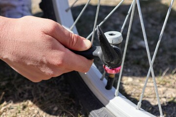 A hand holds a hose of a bicycle pump near the wheel