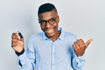 Young african american man holding removable memory usb pointing thumb up to the side smiling happy with open mouth