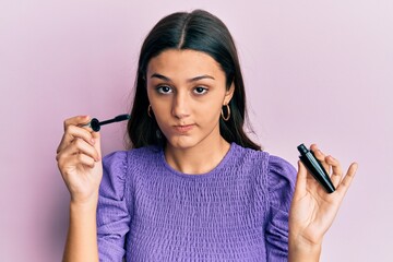 Young hispanic woman holding eyelashes curler skeptic and nervous, frowning upset because of...