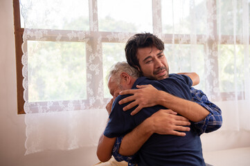 Caucasian senior father comforting and hugging depressed adult son in the bedroom. Elderly dad...