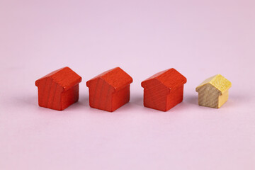 Three red toy houses and one wooden toy house on a pink background. Selective focus.