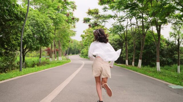 4k slow motion back view of Beautiful happy Asian girl running on road in park lovely young woman running turn back smile at camera free joyful people enjoy the day