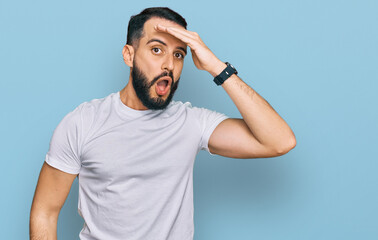 Naklejka premium Young man with beard wearing casual white t shirt surprised with hand on head for mistake, remember error. forgot, bad memory concept.