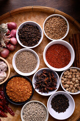 Various dry spices and herbs in a bowl on bamboo tray. Asian food ingredients (chili, clove, caraway, coriander seed, star anise, cardamom, pepper, cinnamon, garlic and shallot)