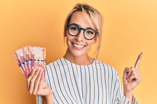 Beautiful blonde woman holding south african 50 rand banknotes smiling happy pointing with hand and finger to the side