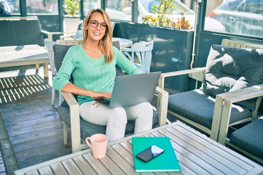 Young blonde woman smiling happy working using laptop sitting at the coffee shop terrace.