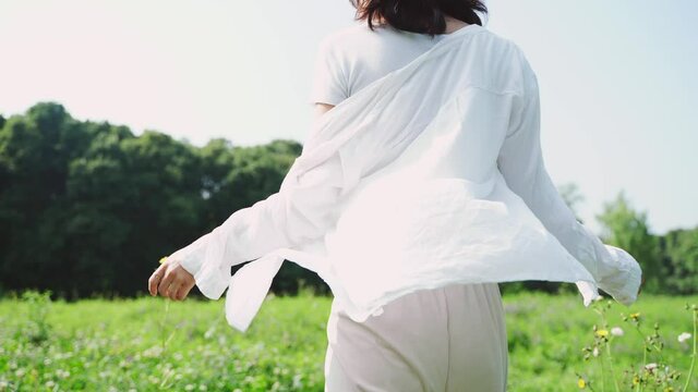 back view 4k slow motion of pretty young slim asian woman in white shirt walking in the blooming spring flower field outdoor in the early summer day charming girl enjoy relax in the nature