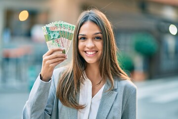 Young latin businesswoman smiling happy holding hong kong dollars at the city.