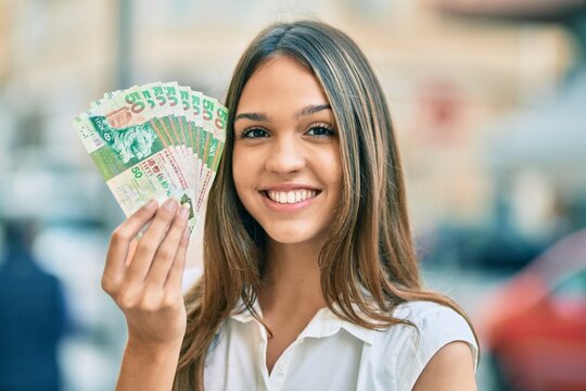 Beautiful latin teenager girl smiling happy holding hong kong dollars at the city.