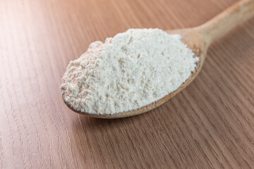 Wooden spoon with wheat flour on wooden table