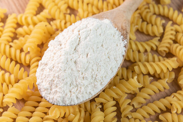 Wooden spoon with wheat flour over raw pasta