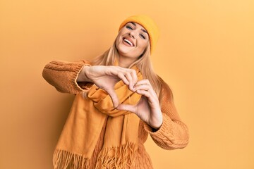 Young caucasian woman wearing wool winter sweater and cap smiling in love doing heart symbol shape with hands. romantic concept.