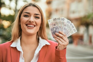 Young blonde businesswoman smiling happy holding polish zloty at the city.
