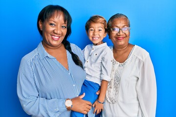 Hispanic family of grandmother, mother and son hugging together looking positive and happy standing and smiling with a confident smile showing teeth