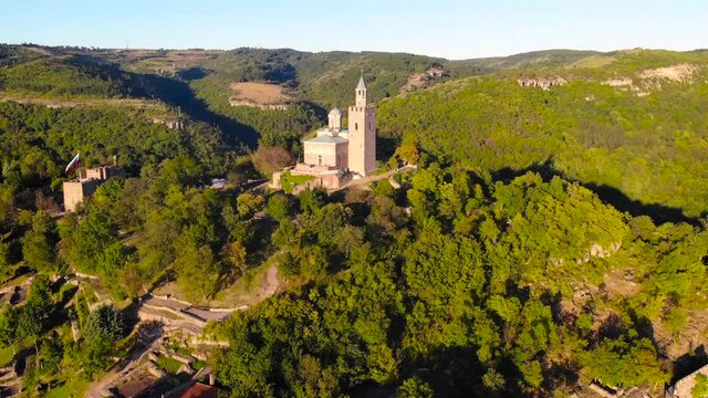 European historic Tsarevets Fortress between the winding rivers and mountains with trees of Veliko Tarnovo, Bulgaria. Beautiful scene of medieval castel took with aerial drone 4K 30fps.