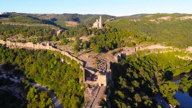 European historic Tsarevets Fortress between the winding rivers and mountains with trees of Veliko Tarnovo, Bulgaria. Beautiful scene of medieval castel took with aerial drone 4K 30fps.